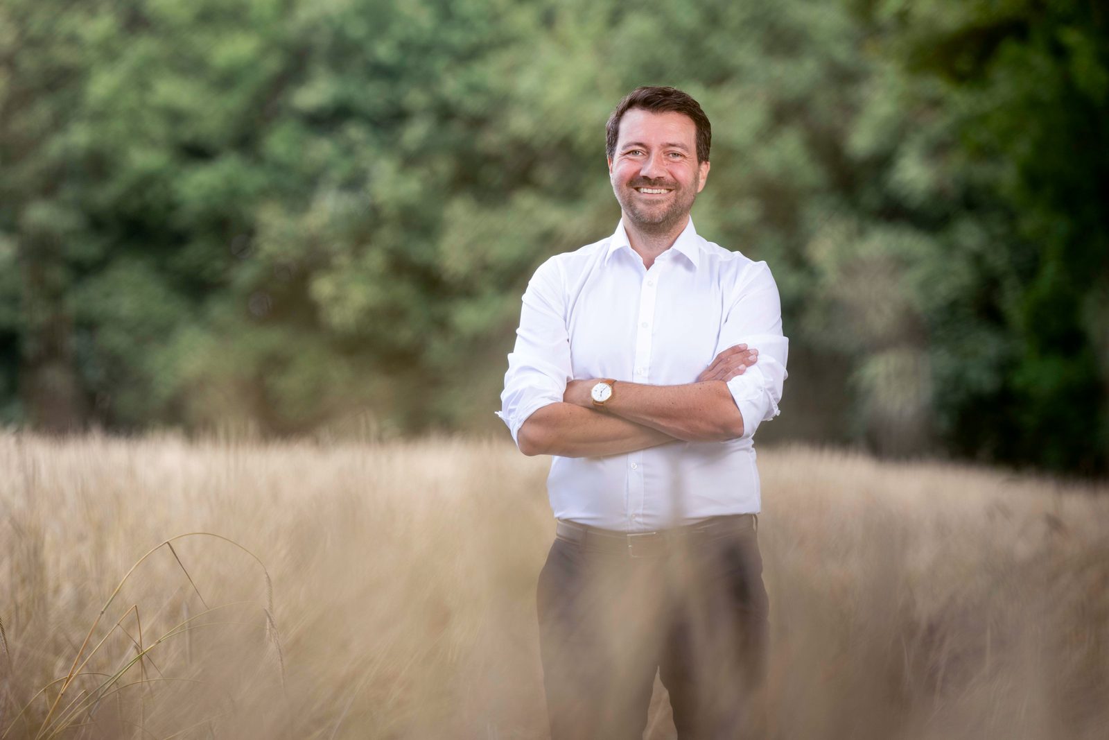 Jochen Steinkamp steht mit verschränkten Armen in einem Getreidefeld vor einem Waldrand