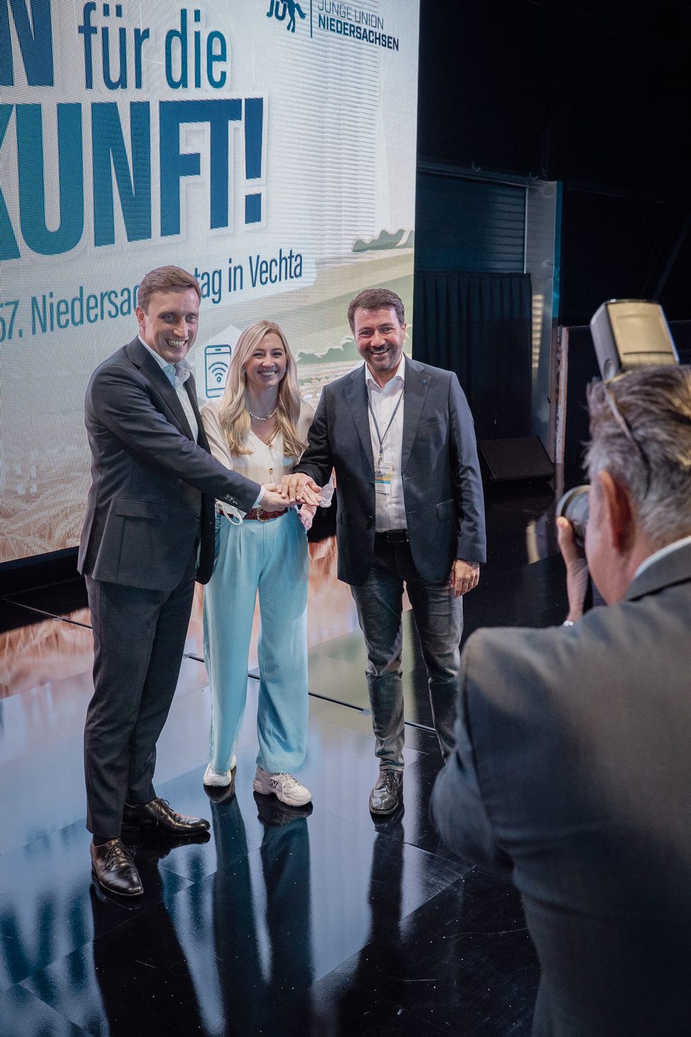 Jochen Steinkamp (rechts) reicht auf der Bühne des Niedersachsentags der Jungen Union in Vechta zwei Mitstreitern die Hand, im Vordergrund ein Fotograf
